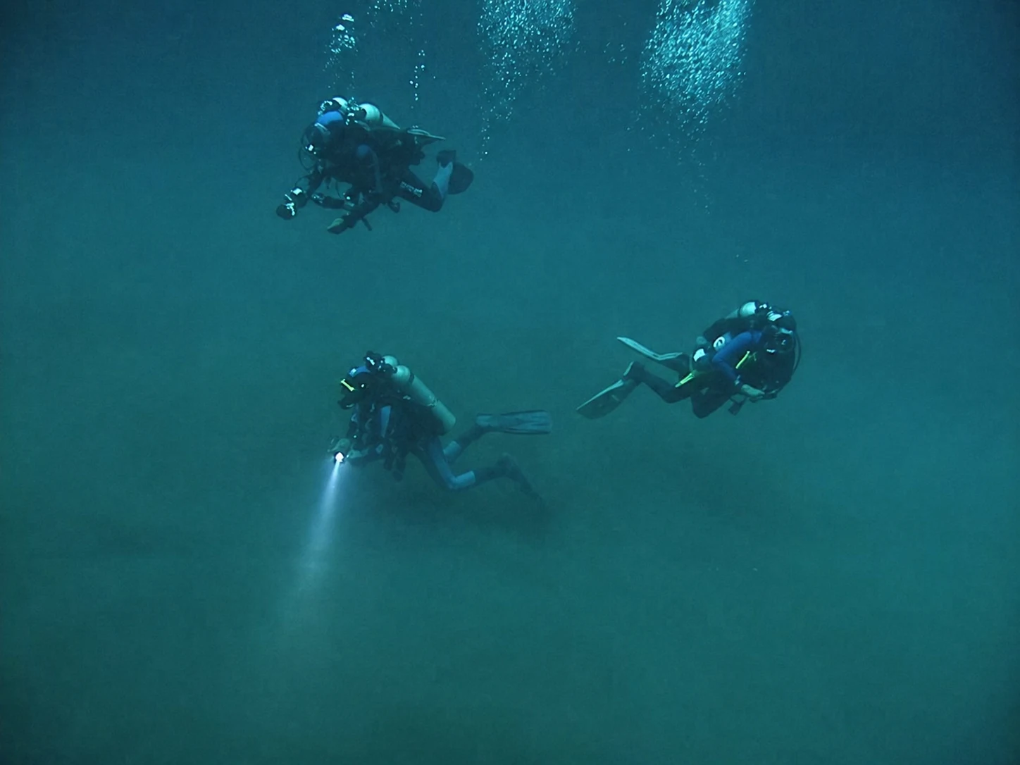 Divers descending with lights in the blue water of Cenote Angelita